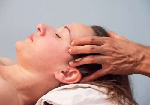 cabeza de una mujer estirada sobre una almohada Nicolas Dréan realiza un masaje en sus sienes apretando puntos de acupuntura